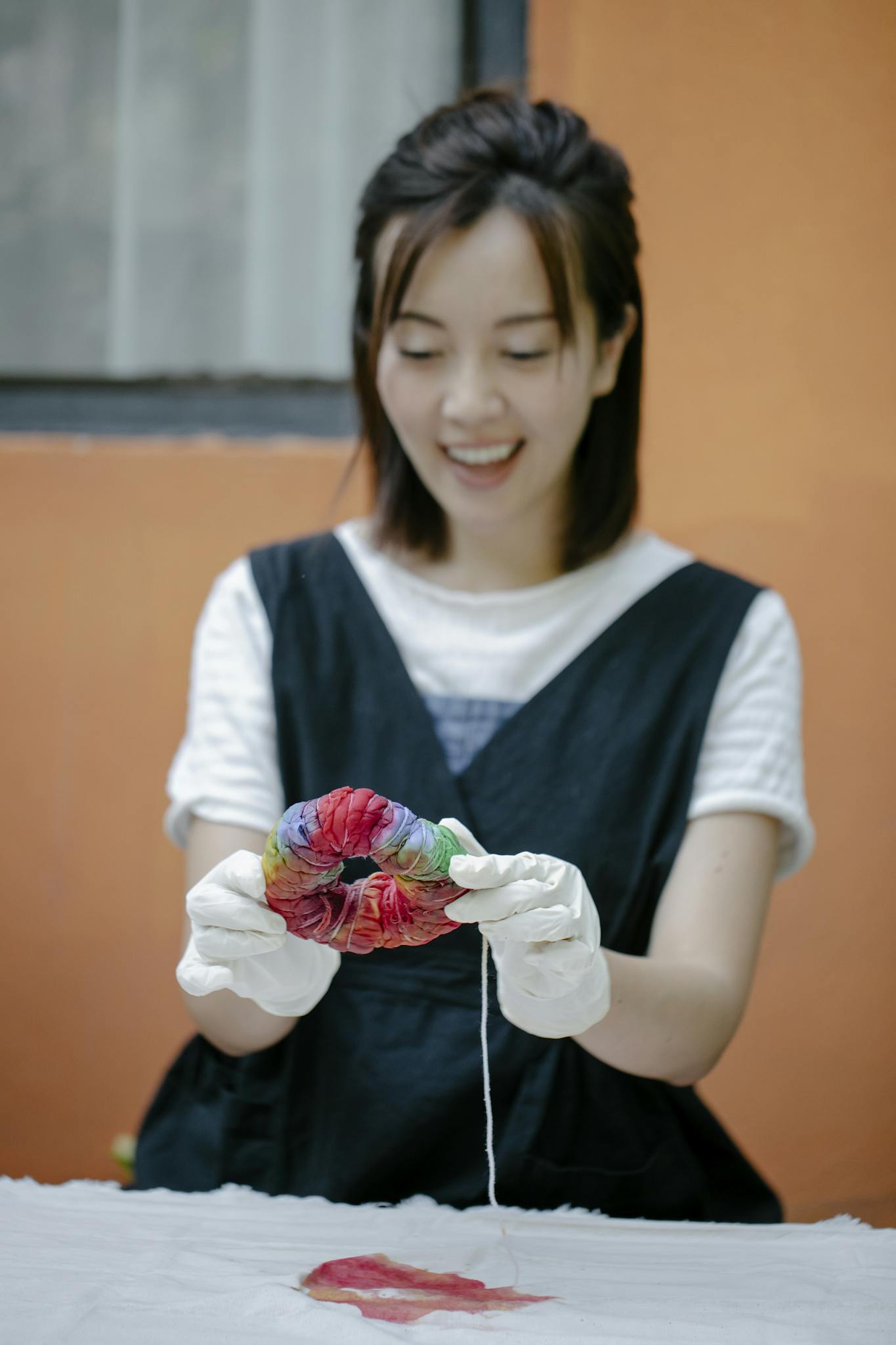 Smiling woman in gloves creating colorful tie-dye fabric indoors.