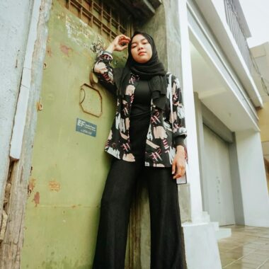 Stylish woman in hijab poses confidently against urban backdrop in Cirebon, Indonesia.