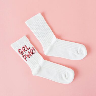 White socks on a pink background featuring empowering feminist slogan "Grl Pwr" in bright embroidery.